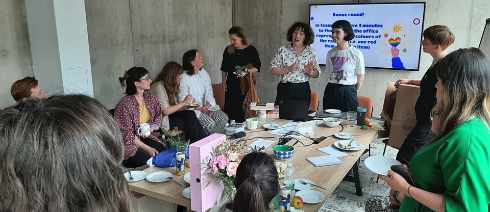 Staff are gathered around a table, participating in a Pride Month quiz ran by our Rainbow Network