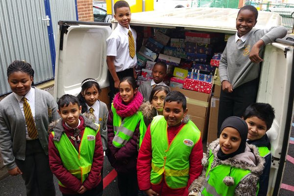 11 school children from a Refugee Welcome school stand smiling around a van filled with presents and gifts