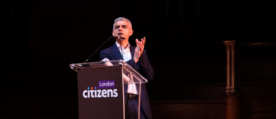 Sadiq Khan standing on stage clapping behind a podium which says London Citizens